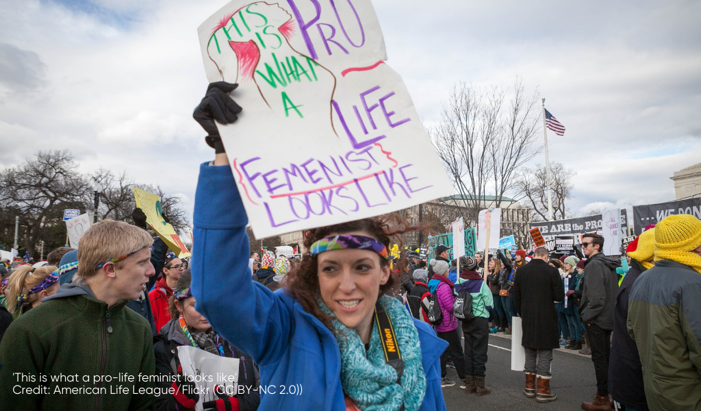 A woman holds up a sign that says 'this is what a pro-life feminist looks like'